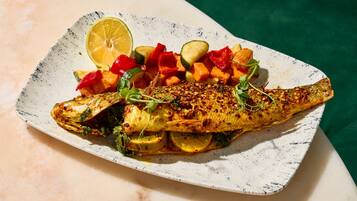 A plate of grilled fish with vegetables and a slice of lime.