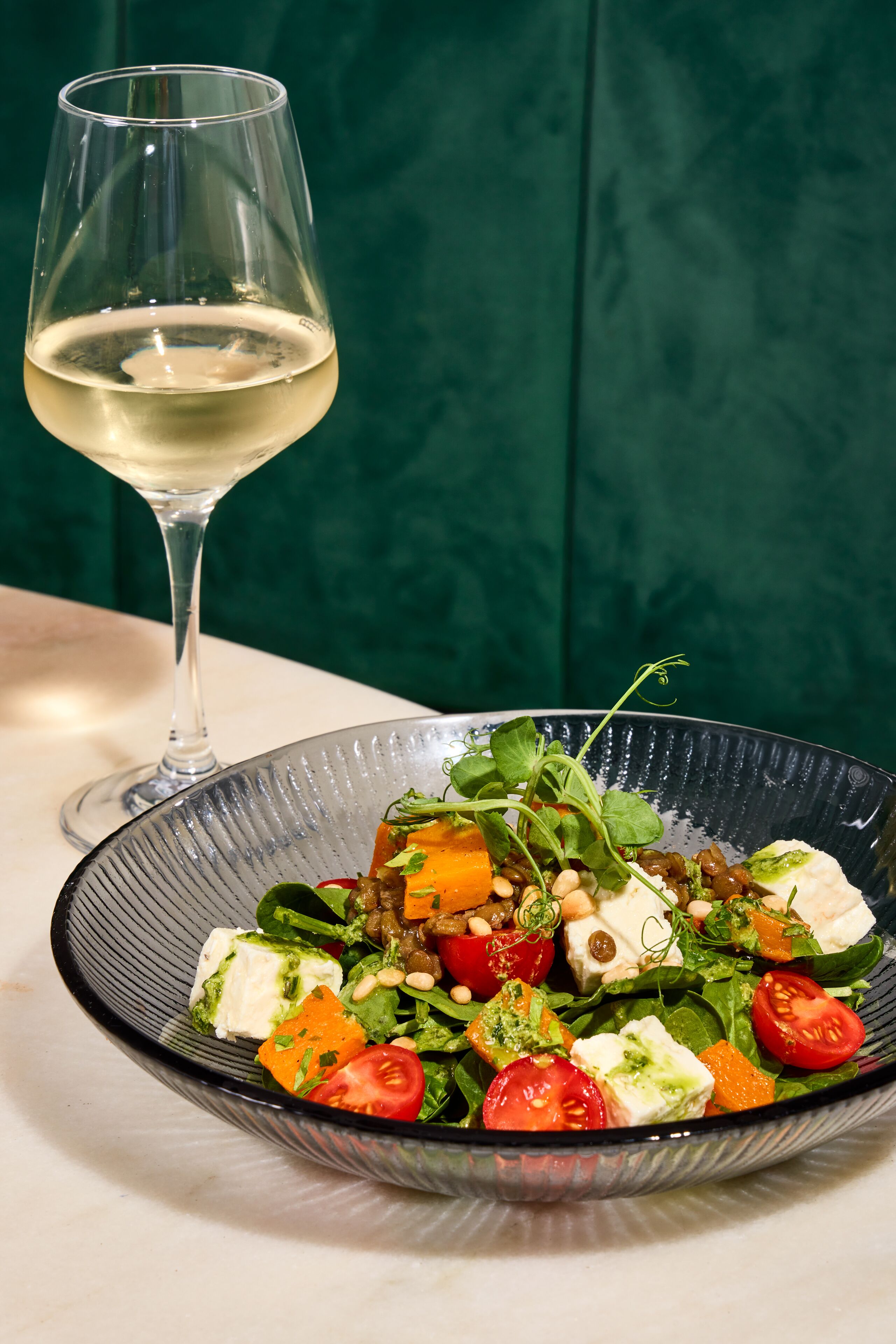 Un verre à vin transparent et un saladier rempli d’une salade composée de divers ingrédients.