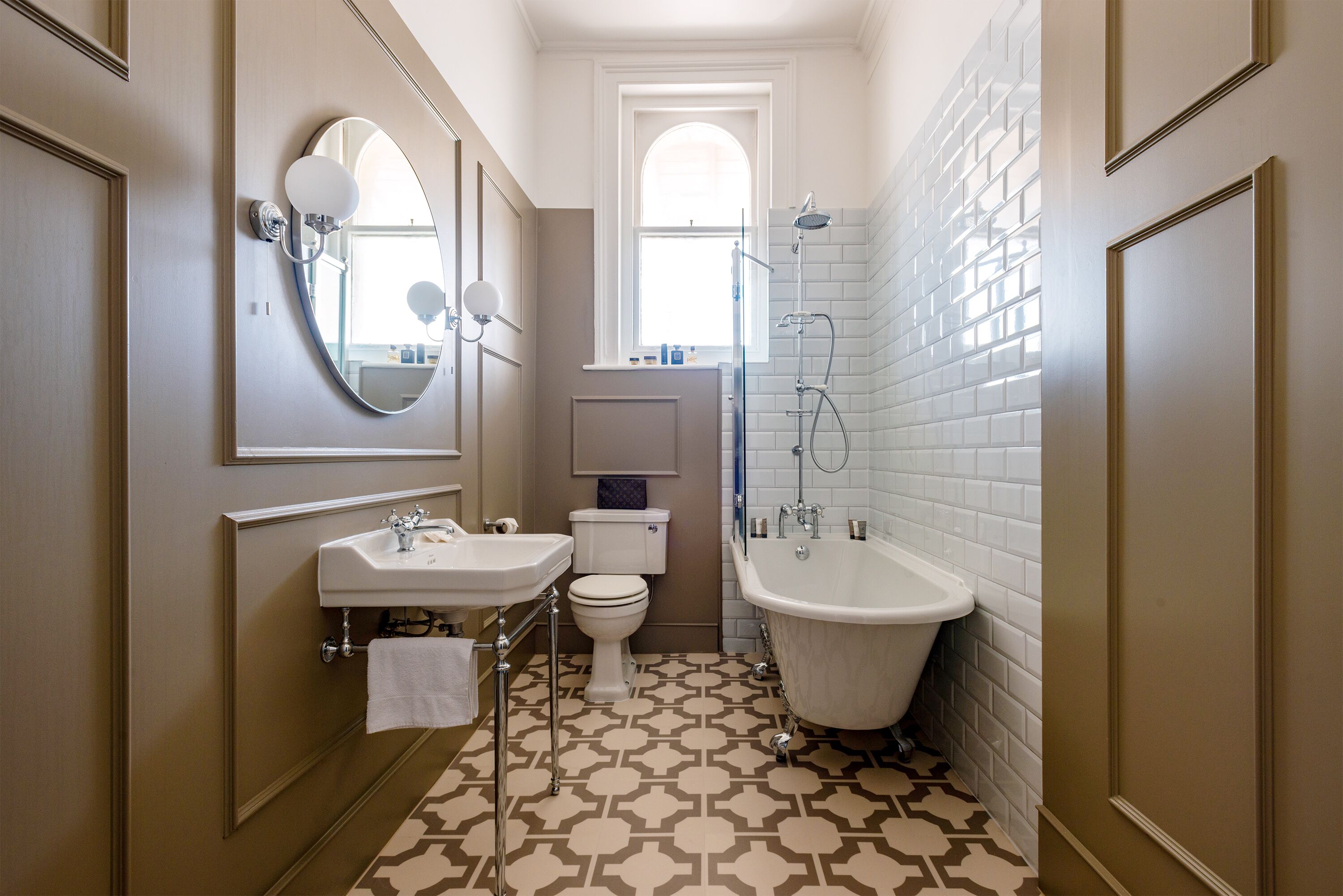 Ein Badezimmer mit Toilette, Waschbecken und Badewanne, mit einem Musterfliesenbelag und einem Fenster.