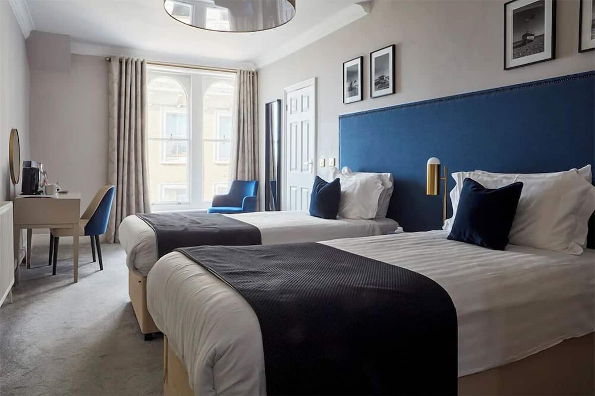 A hotel room with two beds, a desk, a chair, and a large window with curtains.