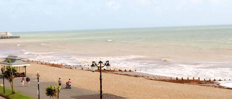 A beach with a promenade, a pier in the background, and a gazebo.
