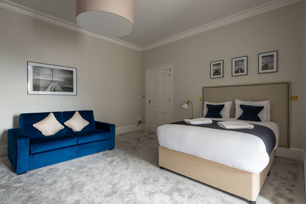 A bedroom with a large bed, a blue sofa, and a white door.