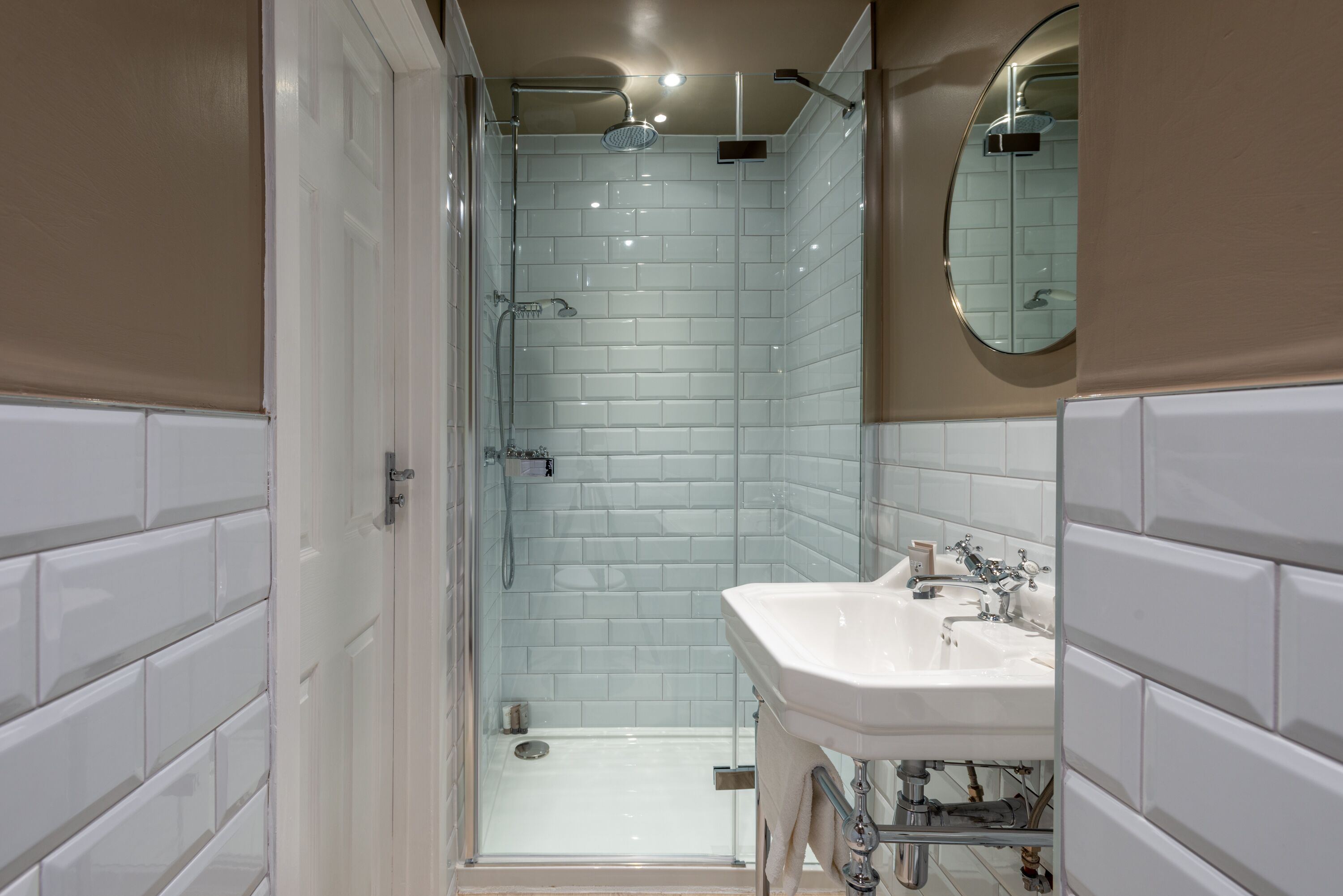 Une salle de bain moderne avec des carreaux de céramique blancs rectangulaires, une douche en verre et un lavabo blanc avec un miroir au-dessus.
