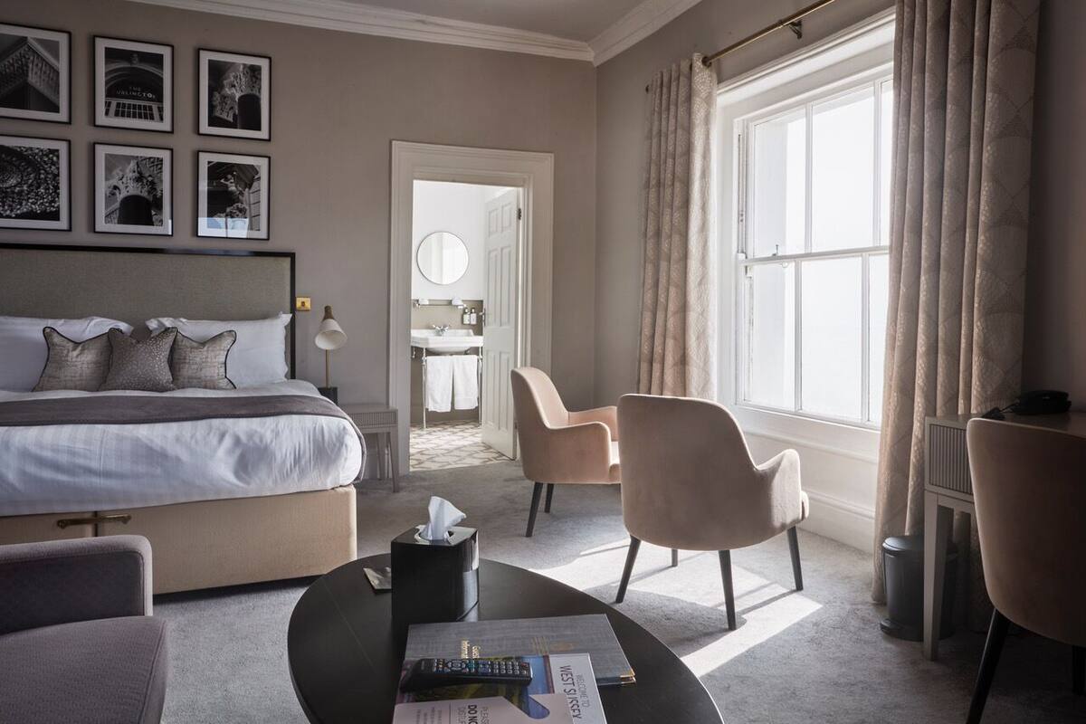 A hotel room with a bed, a desk, two chairs, a coffee table, and a window with curtains.