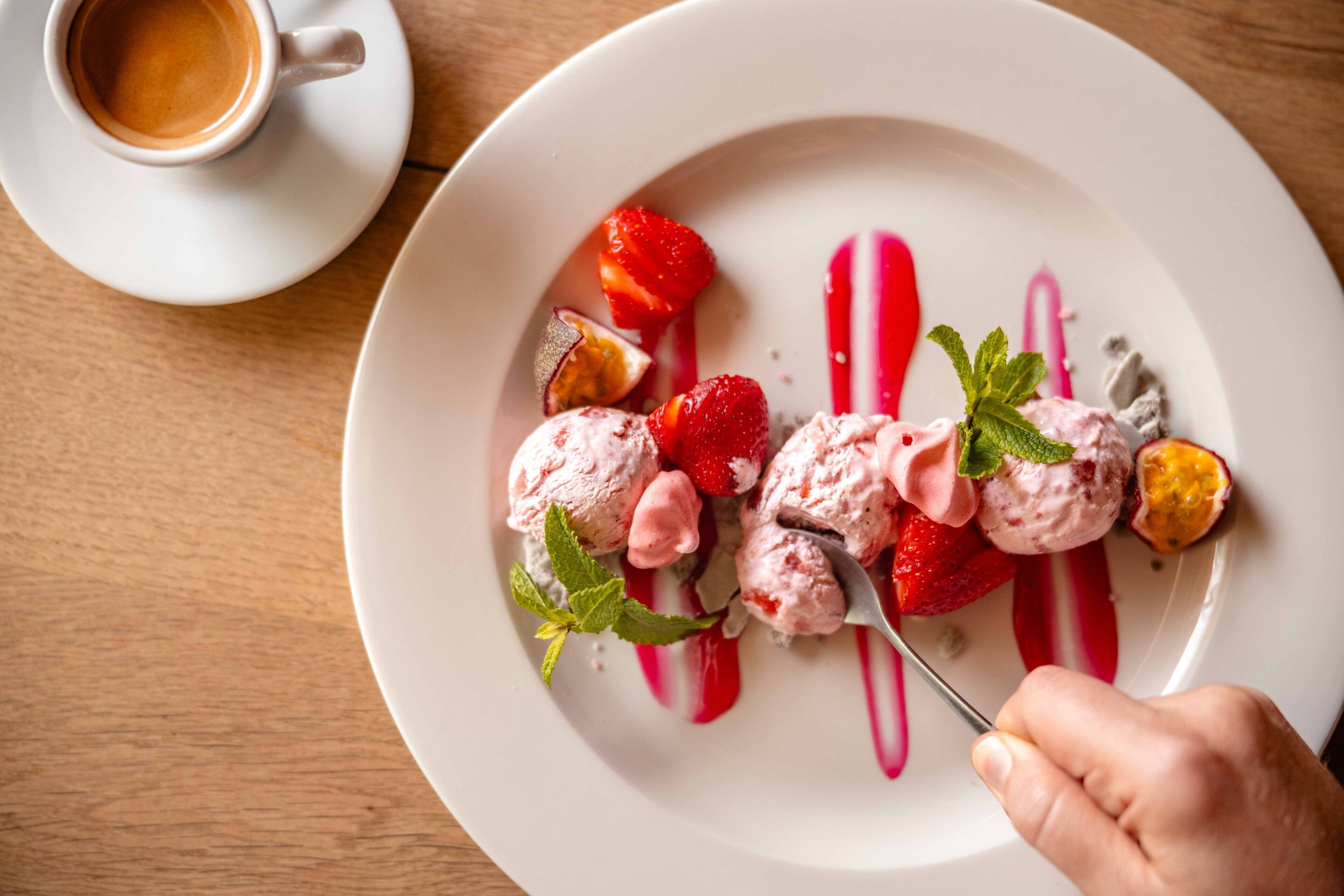 Un plato de postre con helado, fresas y una ramita de menta.