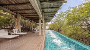 Una terraza de madera con sillones de descanso y una piscina.