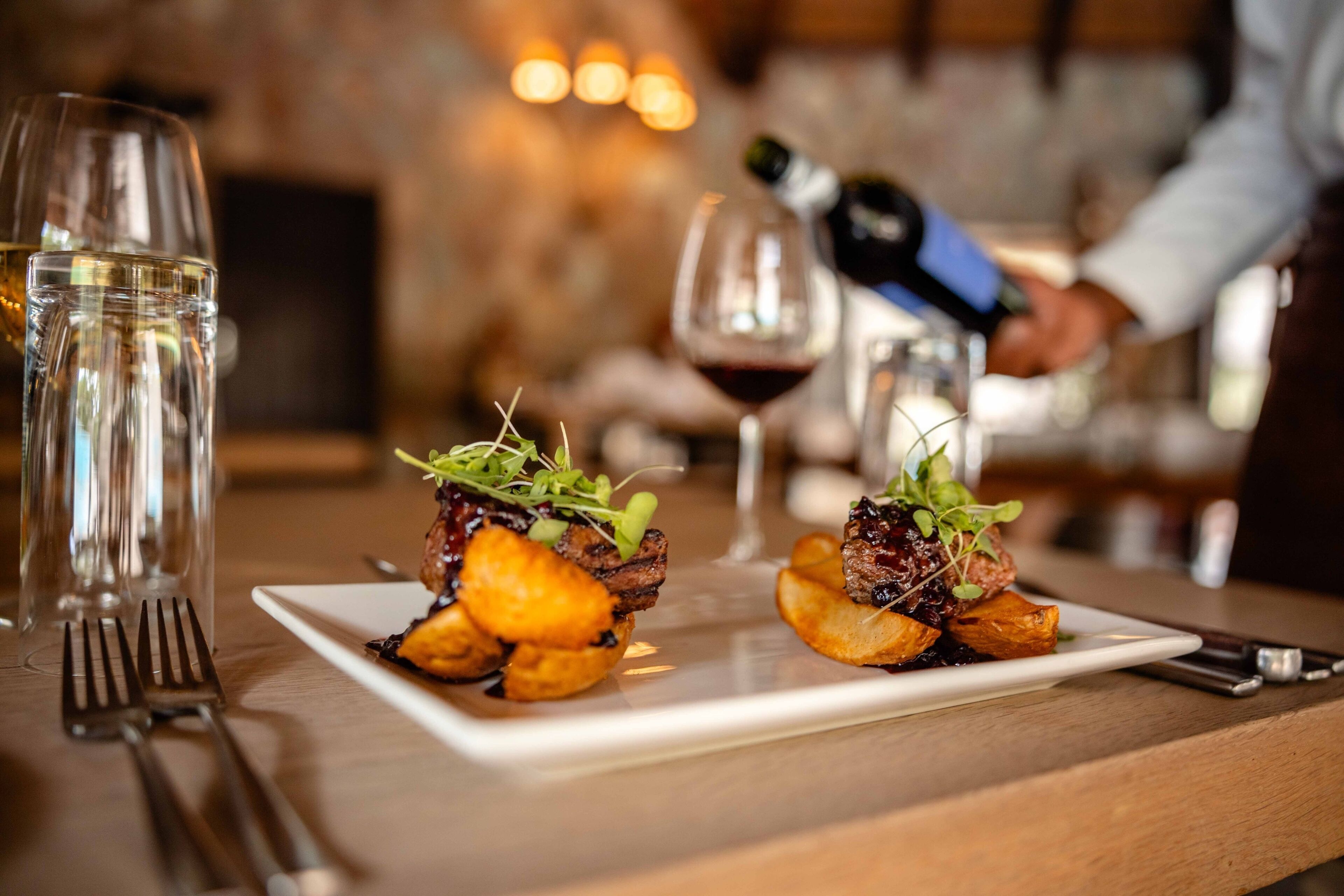 A dining table with two plates of food, a bottle of wine, and a wine glass.