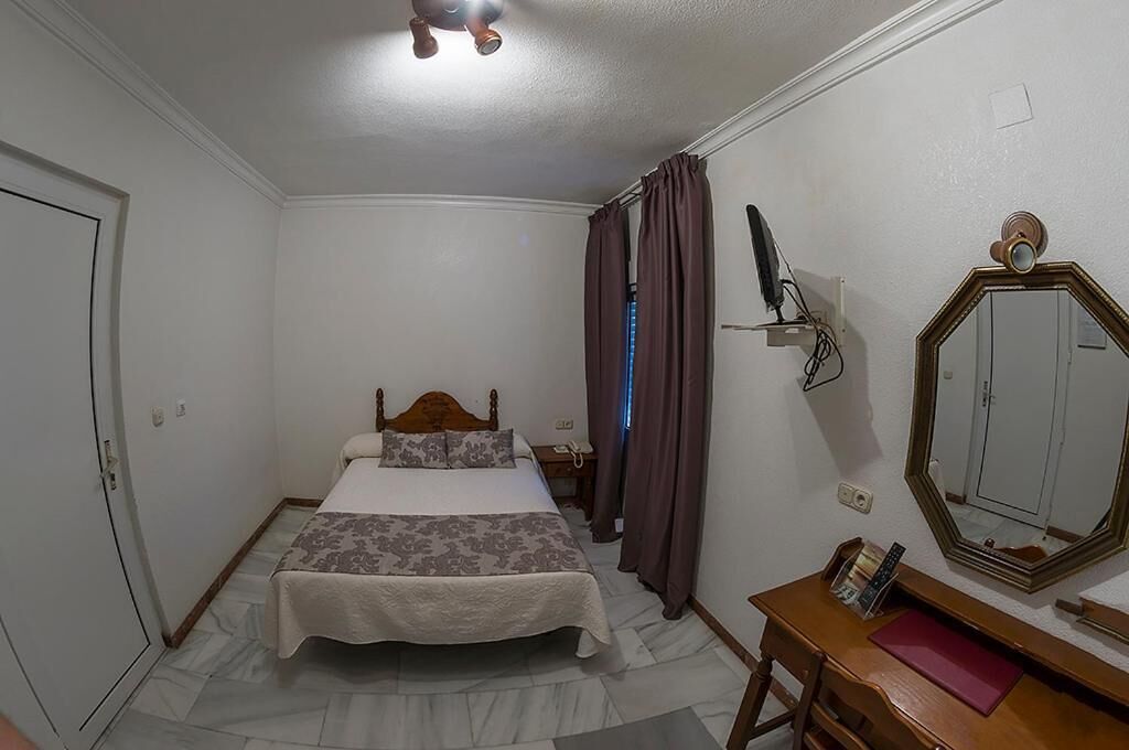 A bedroom with a bed, a bedside table, a mirror, and a wardrobe.