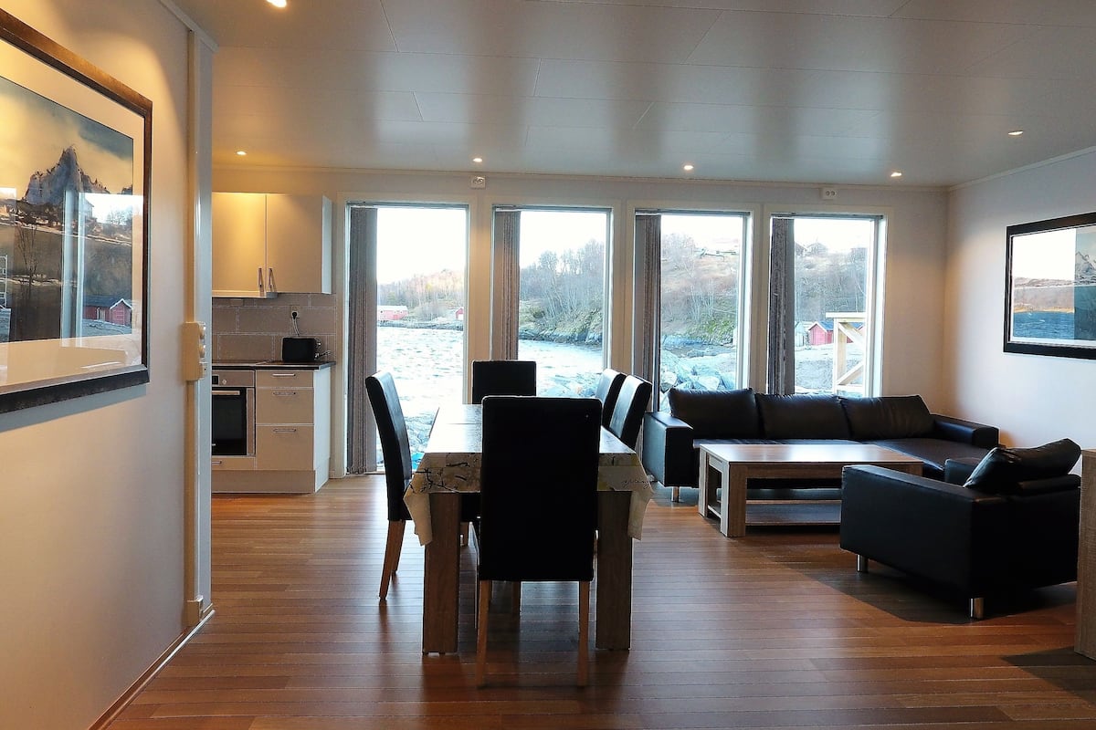 A modern living room with a dining area, large windows, and a view of a snowy landscape.