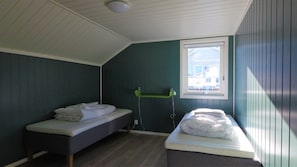 A small, single-room accommodation with two beds, a window, and a ceiling fan.