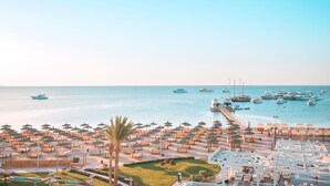 Ein Yachthafen mit vielen Booten, ein Strandabschnitt mit Sonnenschirmen und Liegestühlen und freie Sicht auf das Meer.