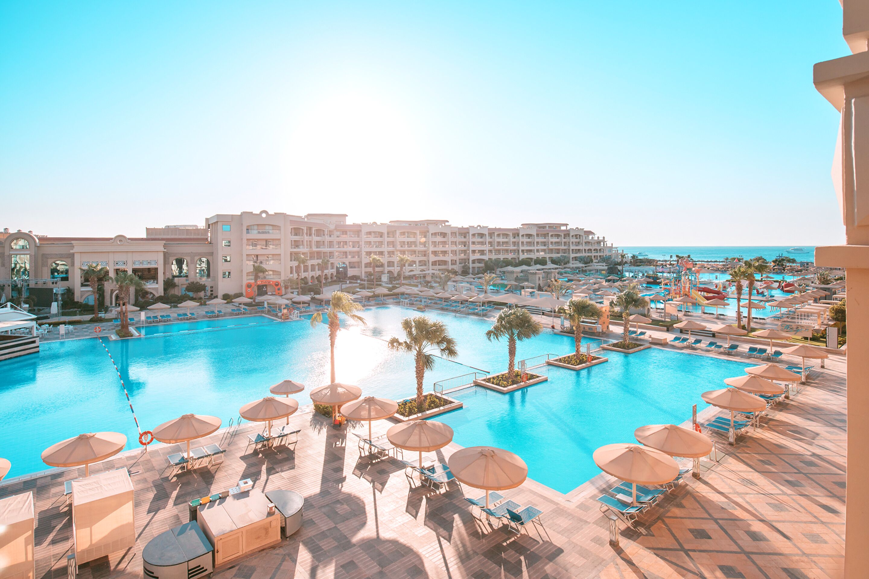 Ein Resort mit großem Pool, Liegestühlen, Sonnenschirmen und Meerblick.