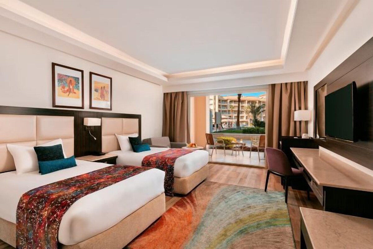 Une chambre d’hôtel avec deux lits, un bureau, une chaise, une télévision et une vue sur la ville.