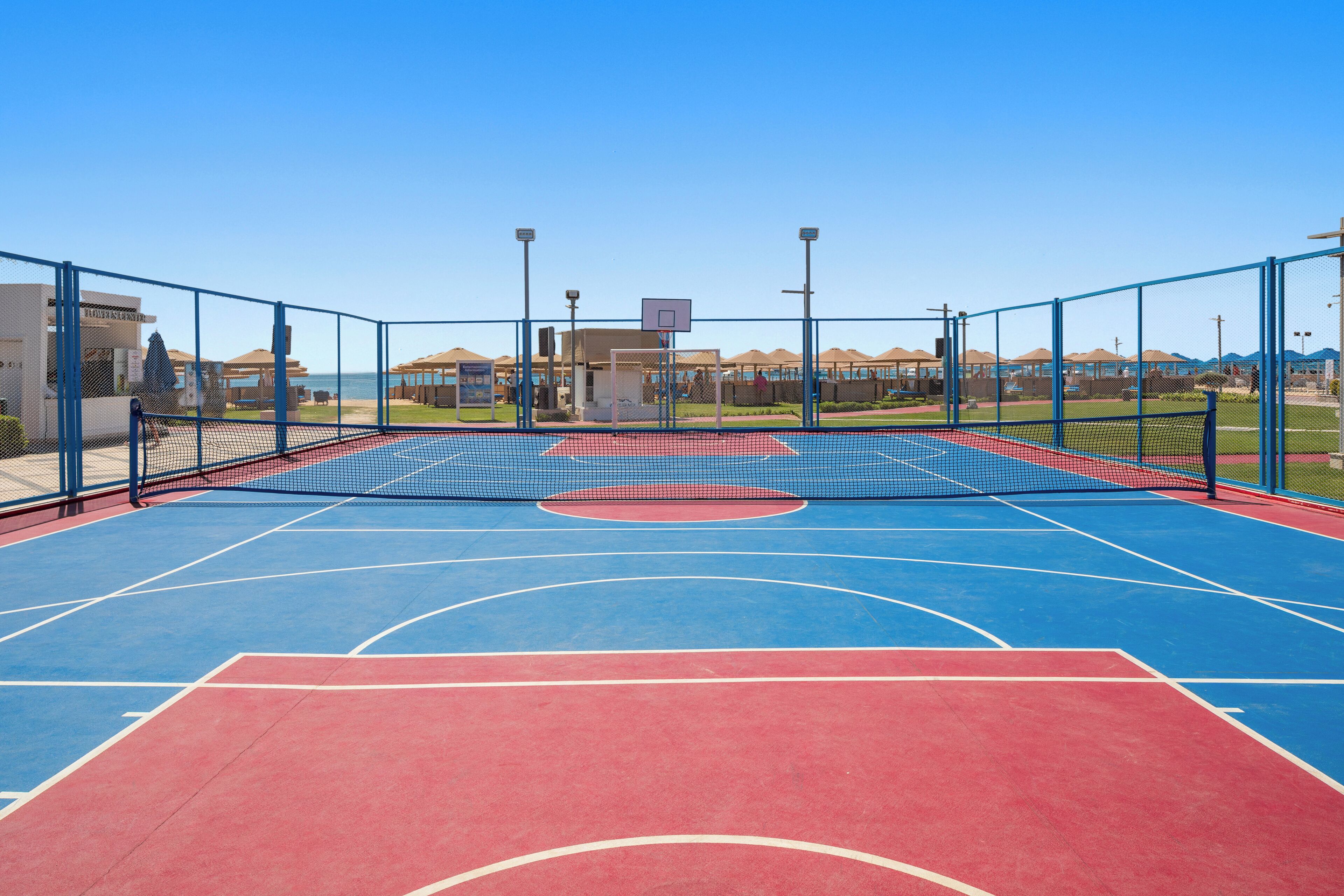 Ein Basketballplatz im Freien mit Netz, umgeben von einem Zaun, und ein Gebäude im Hintergrund.
