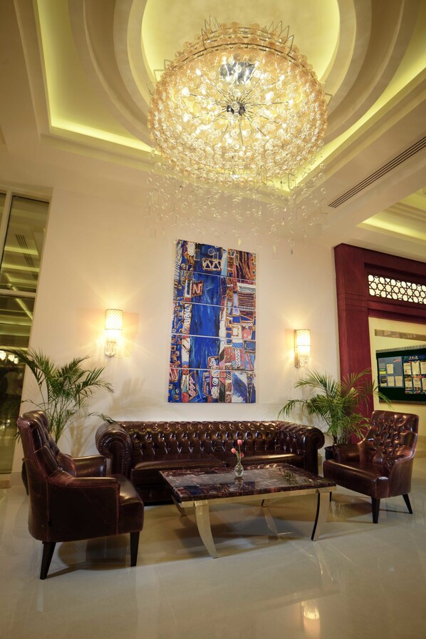 A lobby with a large, ornate chandelier, a colorful abstract painting, and a seating area with leather sofas and armchairs.
