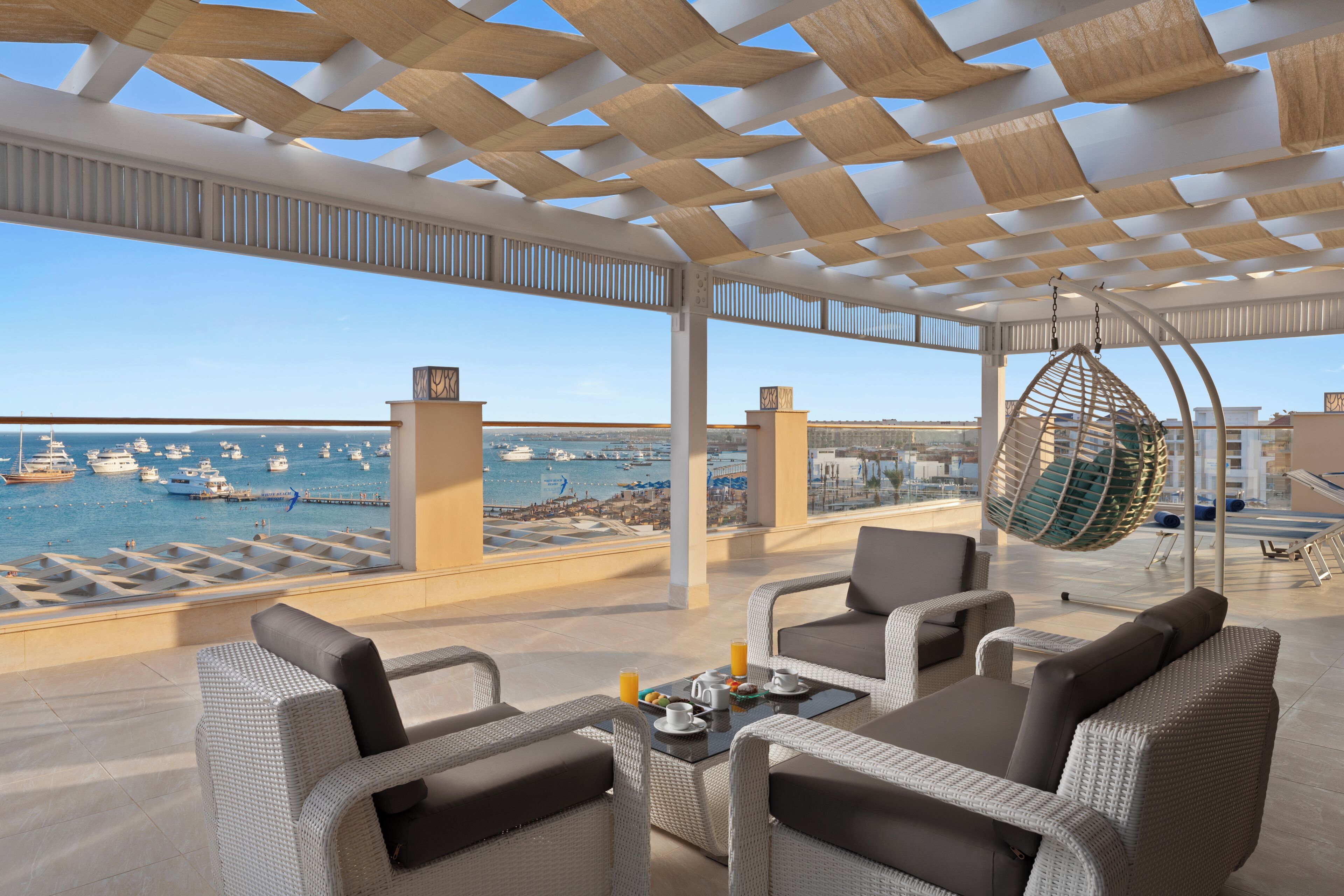 Eine Dachterrasse mit Korbmöbeln, einer Hängematte und Blick auf Boote in einer Marina.