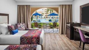 Ein Hotelzimmer mit Bett, Schreibtisch, Stuhl und Blick auf ein Schwimmbad und Palmen.