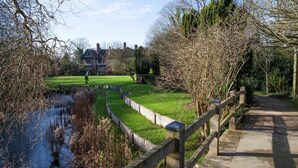 A pathway leading to a grassy area with a pond, surrounded by trees and a building in the background. - Robinson College - Cambridge University - Campus Accommodation (Cambridge)