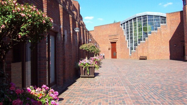 A courtyard with brick buildings, a curved glass structure, and potted plants. - Robinson College - Cambridge University - Campus Accommodation (Cambridge)