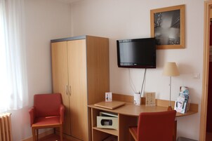 Una habitación de hotel con un armario de madera, un escritorio con lámpara, un televisor y un revistero.