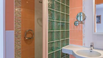 A bathroom with a glass shower enclosure, a sink with a mirror, and patterned tiles on the walls.
