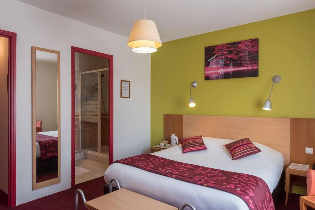 A hotel room with a bed, bedside tables, a mirror, a door, and a painting on the wall.