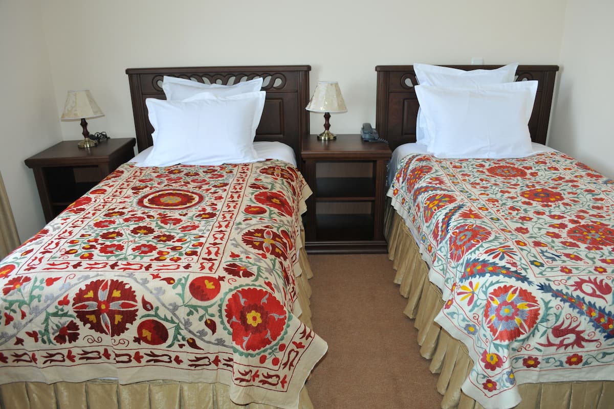 Two single beds with floral bedspreads, wooden headboards, bedside tables with lamps, and a carpeted floor.