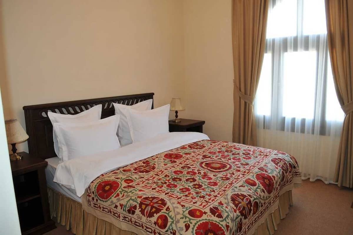 A neatly made bed with a patterned bedspread, a wooden headboard, and a nightstand with a lamp.