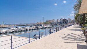 A marina with boats docked, a waterfront promenade, and buildings in the background. - Globales Isabel (Son Servera)