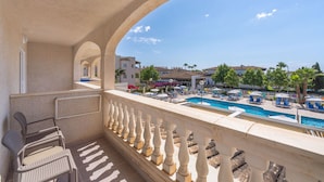 A balcony with a pool view, featuring a poolside area with lounge chairs and umbrellas, and a clear sky. - Globales Isabel (Son Servera)