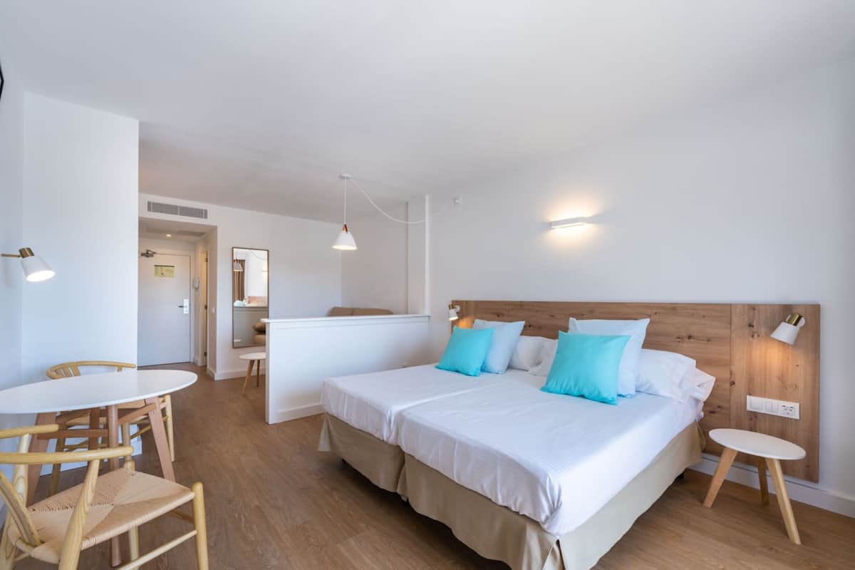 A modern hotel room with a wooden bed, white bedding, a small round table, and a chair.