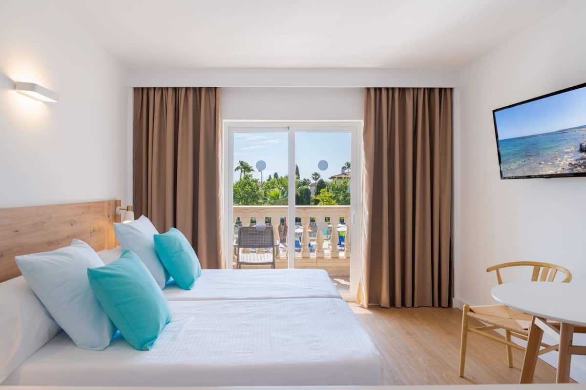 A hotel room with a bed, a TV, a balcony with a view of the sea, and a table with a chair.