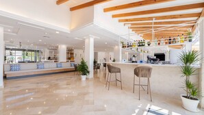 A spacious lobby with a high ceiling, wooden beams, a bar area with stools, and potted plants. - Globales Isabel (Son Servera)
