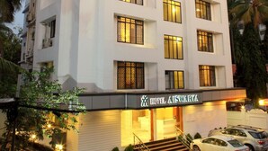 A multi-story hotel with a white facade, a visible entrance with steps, and several parked cars in front. - Hotel Aiswarya (Kanayannur)