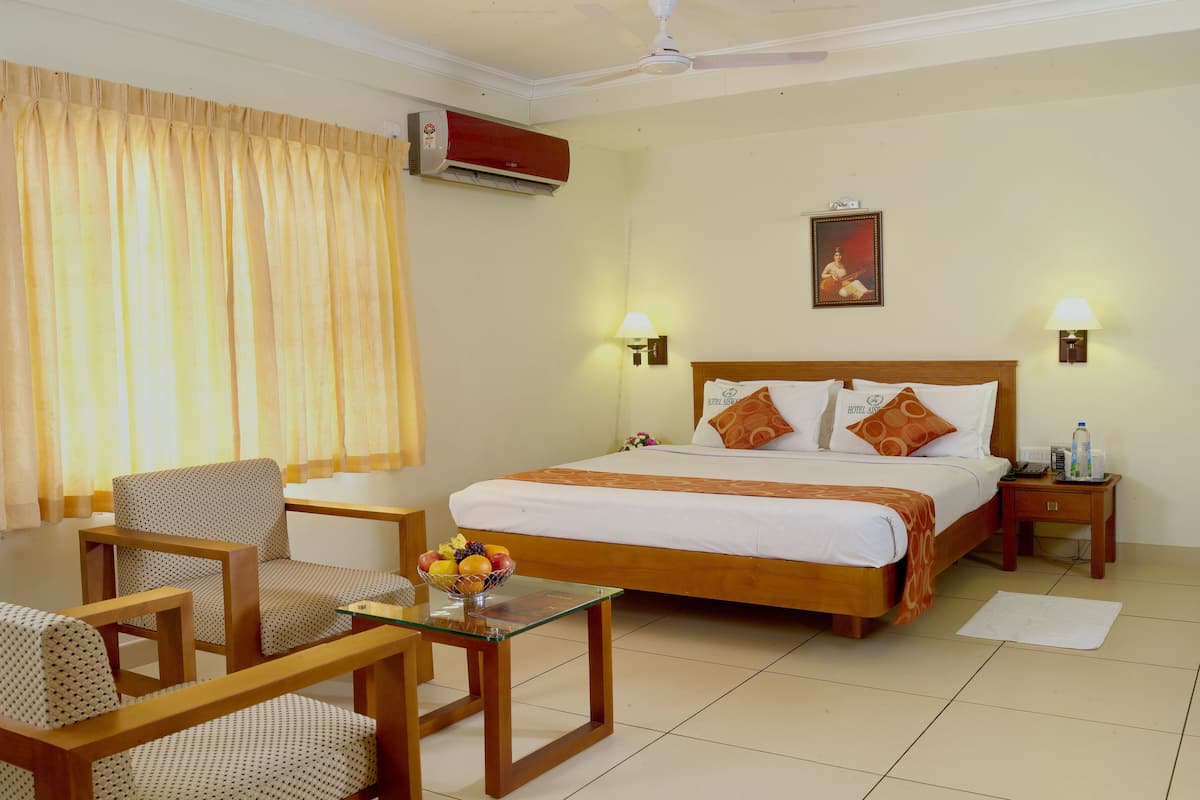 A hotel room with a bed, two bedside tables, a chair, a glass-top table with fruit, and a ceiling fan.