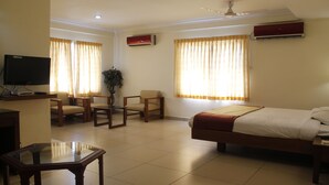A hotel room with a bed, a TV, a desk, and two chairs. - Hotel Aiswarya (Kanayannur)