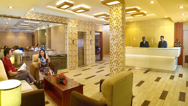 A hotel lobby with a reception desk, seating area, and a restaurant in the background. - Hotel Aiswarya (Kanayannur)