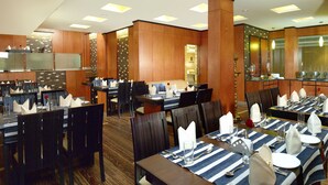 A restaurant with multiple dining tables set for guests, featuring striped tablecloths and neatly arranged cutlery. - Hotel Aiswarya (Kanayannur)