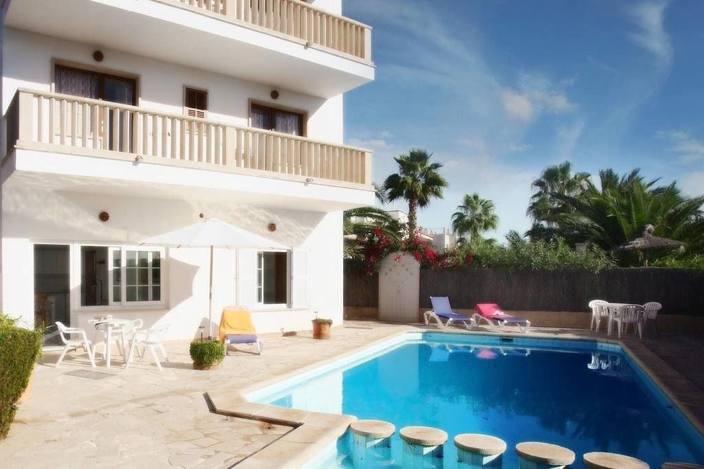 Un edificio de dos pisos con piscina, mobiliario exterior y palmeras.