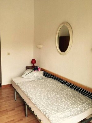 A single bed with a patterned bedspread, a bedside table with a lamp, and a mirror on the wall. - Cala Figuera Apartments (Santanyi)
