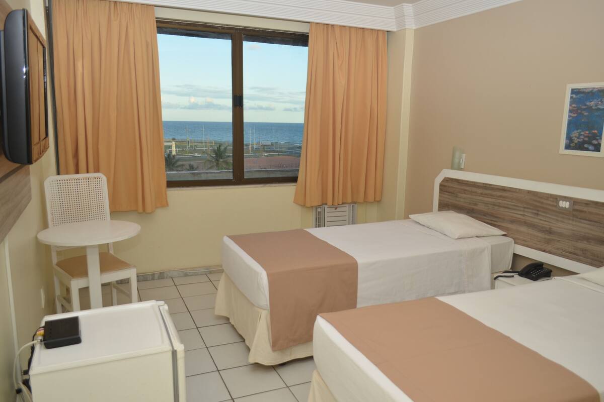 Ein Hotelzimmer mit zwei Betten, einem Fernseher, einem Stuhl und einem Fenster mit Vorhängen.