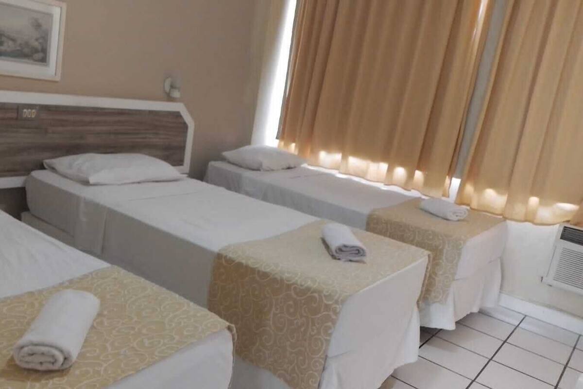 Ein Hotelzimmer mit drei Einzelbetten, auf jedem liegt ein gerolltes Handtuch.