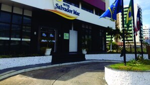 Das Außere des Hotel Salvador Mar mit einem gut sichtbaren Schild, einer gefliesten Eingangsparte und mehreren Flaggen.
