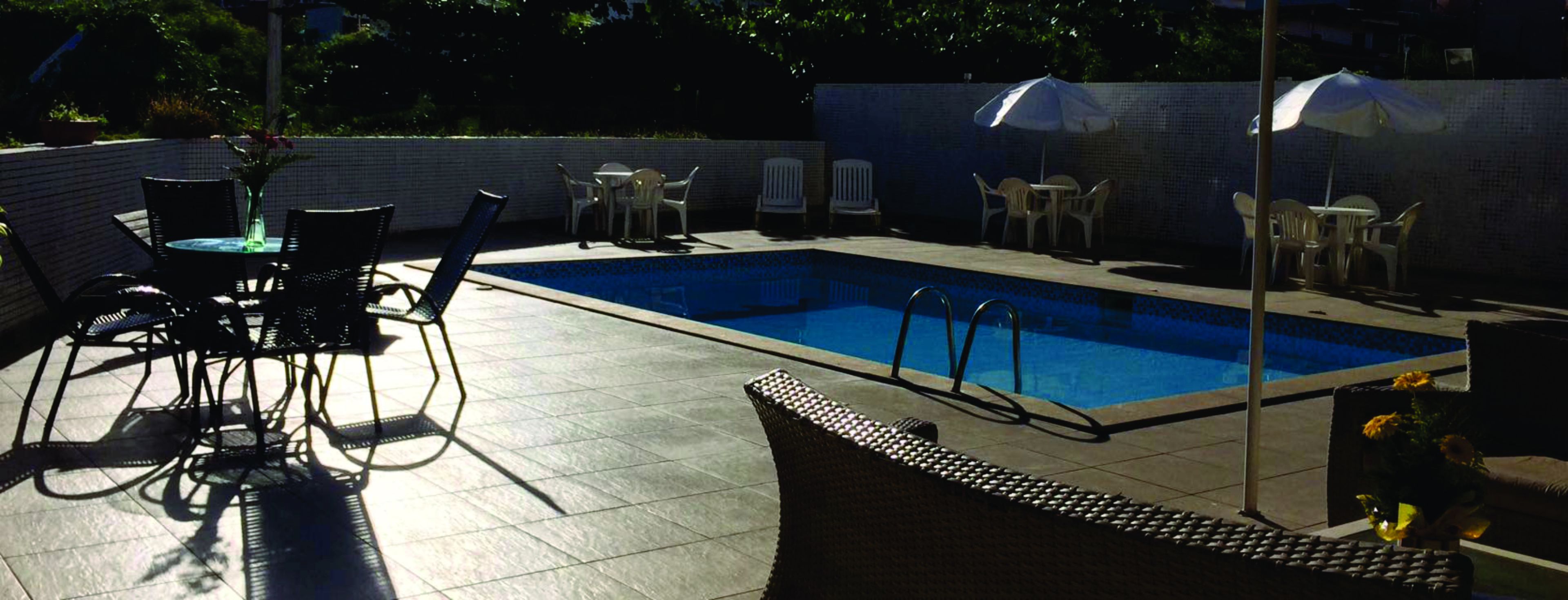 A swimming pool with tiled edges, surrounded by outdoor seating including chairs and tables.