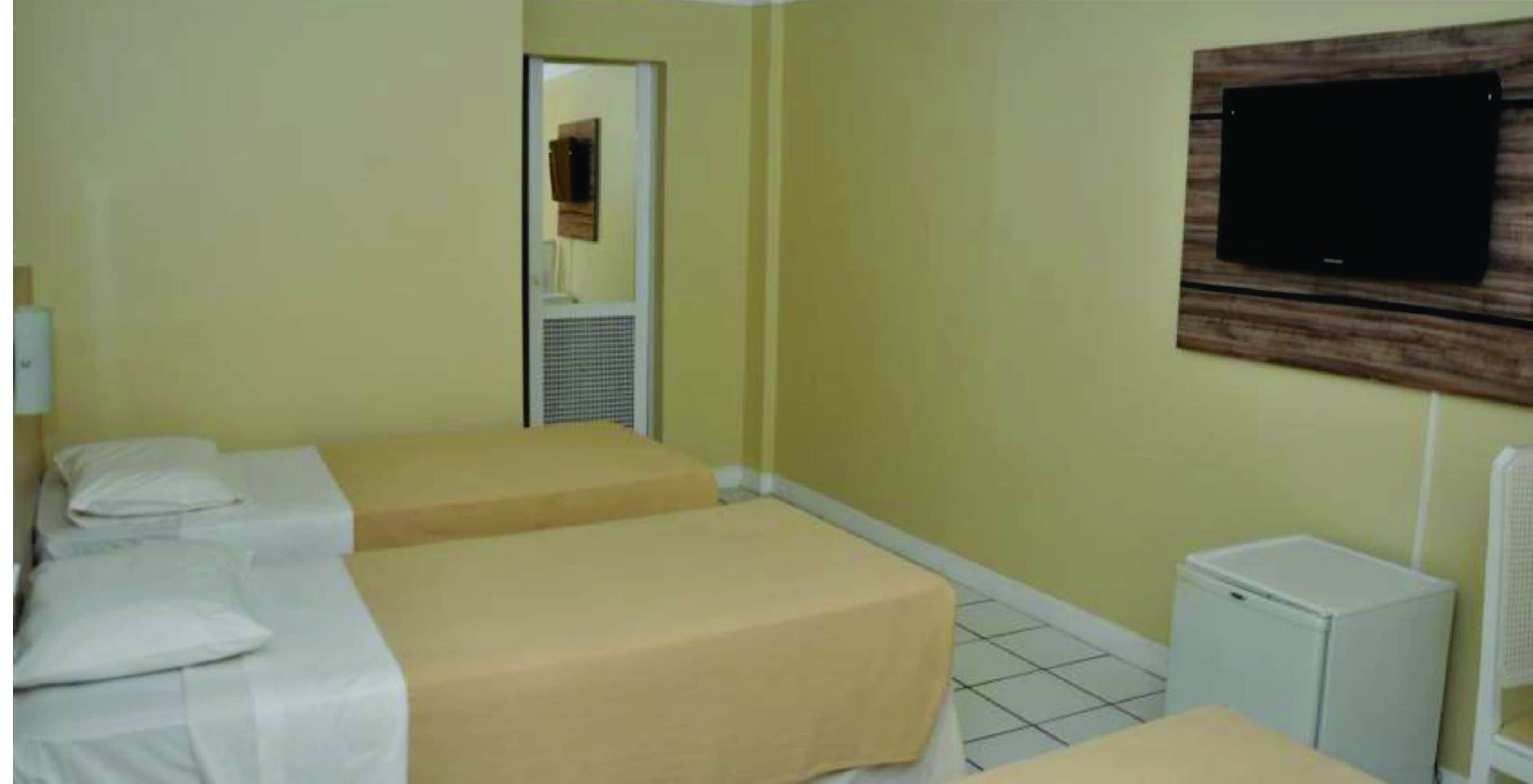 A hotel room with two beds, a television mounted on the wall, and a small white cabinet.