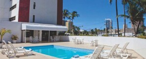 Un hotel con piscina, sillas de descanso blancas y palmeras.