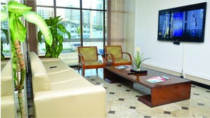 Eine Lobby mit einer Couch, zwei Sesseln, einem Couchtisch, einem Fernseher und großen Fenstern mit Blick auf die Stadt.