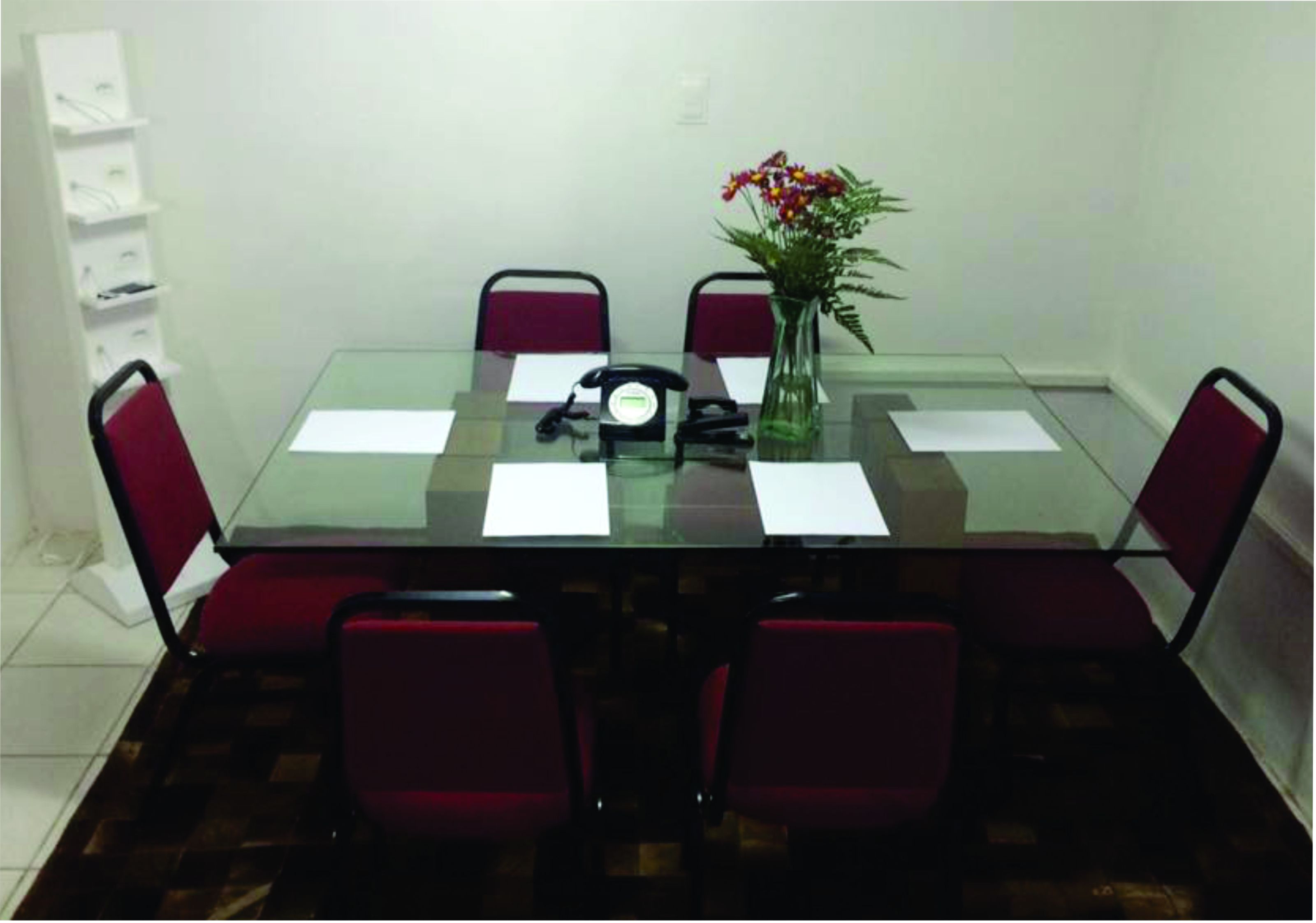 Une table à manger avec un plateau en verre, quatre chaises rouges, un vase avec des fleurs et un téléphone posé sur la table.