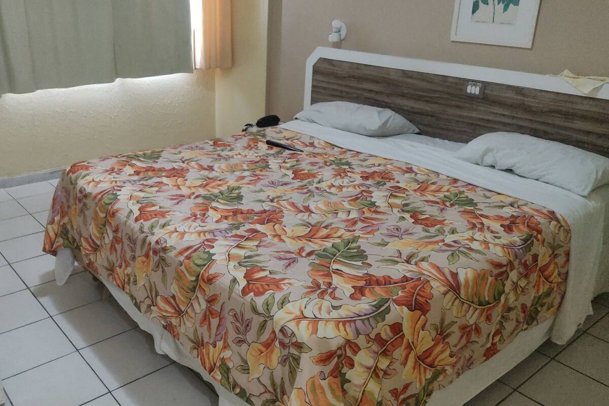 Ein Schlafzimmer mit geblümtem Bettbezug, einem Nachttisch und einem Fenster mit Vorhängen.