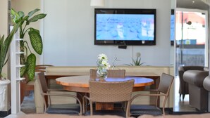 Ein Essbereich mit einem runden Holztisch, Korbstühlen, einer Blumenvase und einem Flachbildfernseher an der Wand.